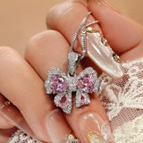 Zircon Bow Pendant Necklace in silver with pink stones, worn by a hand with decorative nails, ideal for bijoux femme.
